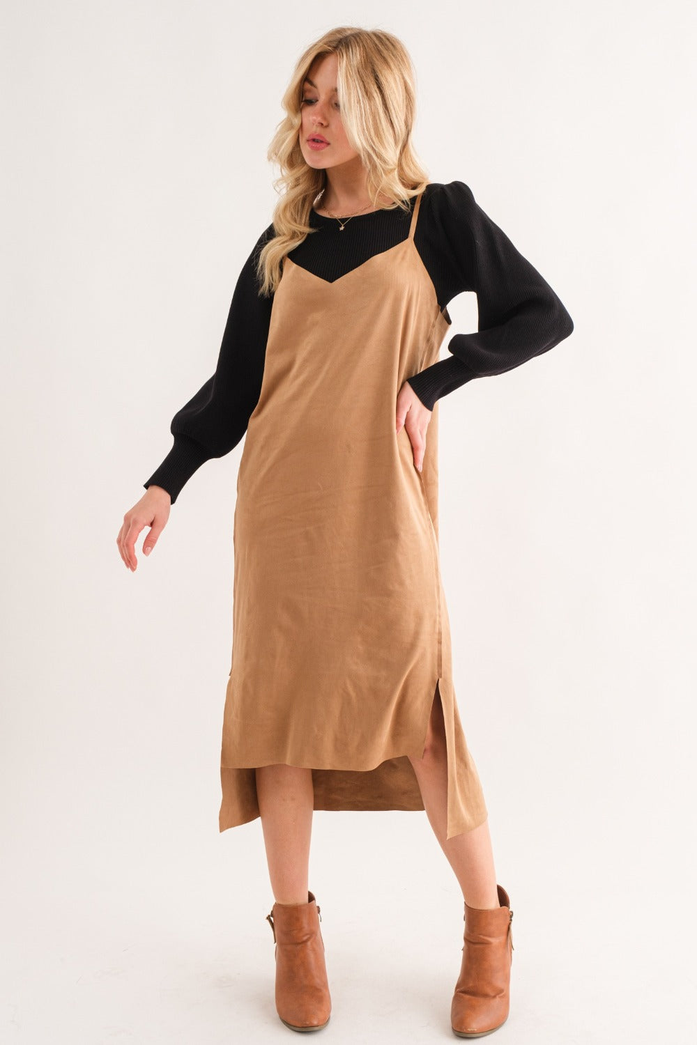 A woman wearing a wide-brimmed hat, black long-sleeve top, and the And The Why Faux Suede Cut Edge Slit Cami Midi Dress poses against a plain background.