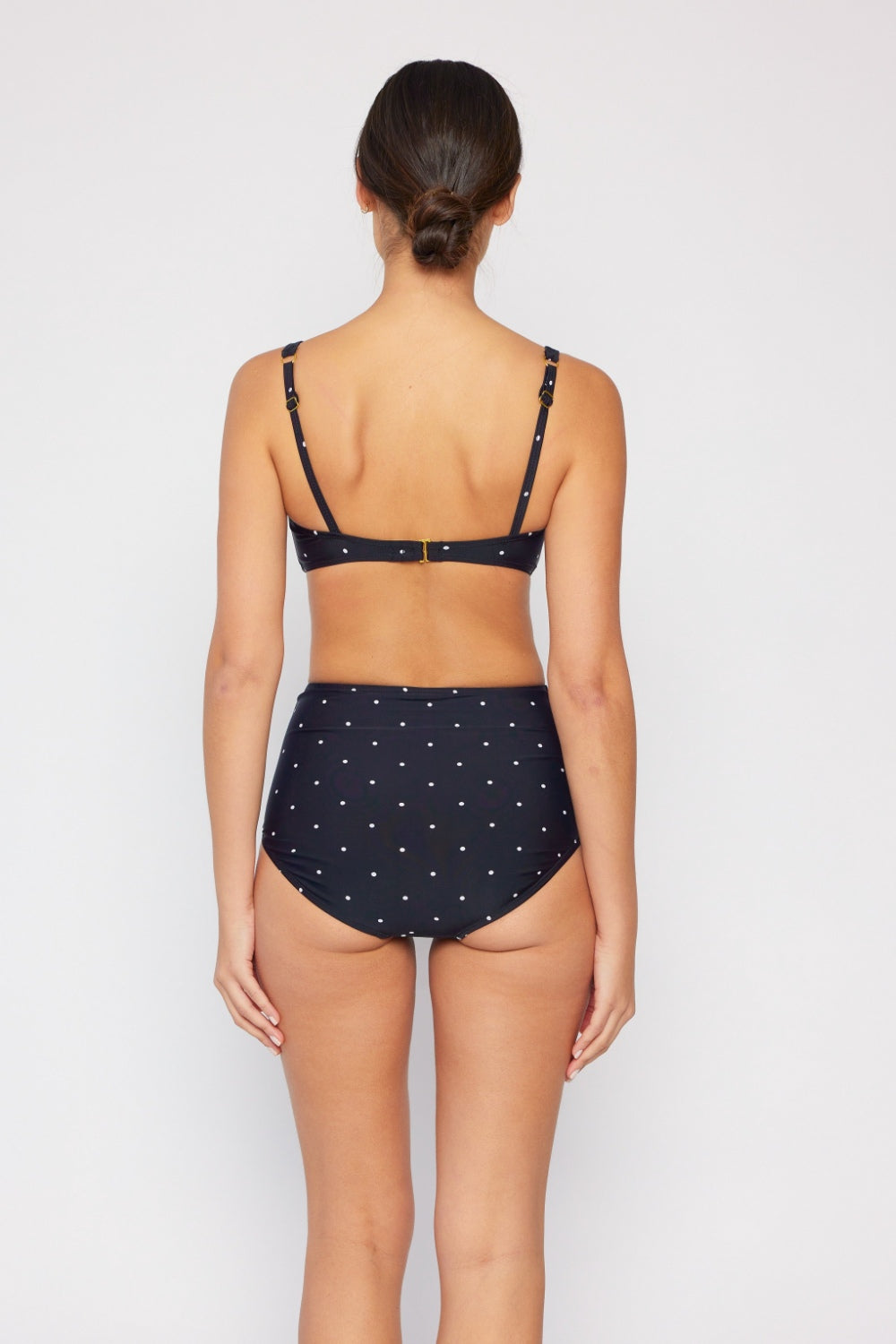 Wearing the fashionable Marina West Swim Take A Dip Twisted High-Rise Bikini Set in black polka dot, one effortlessly combines style with practicality. This chic bikini is complemented by a woven bag with striped handles, set against a neutral backdrop for the ultimate summer vibe.