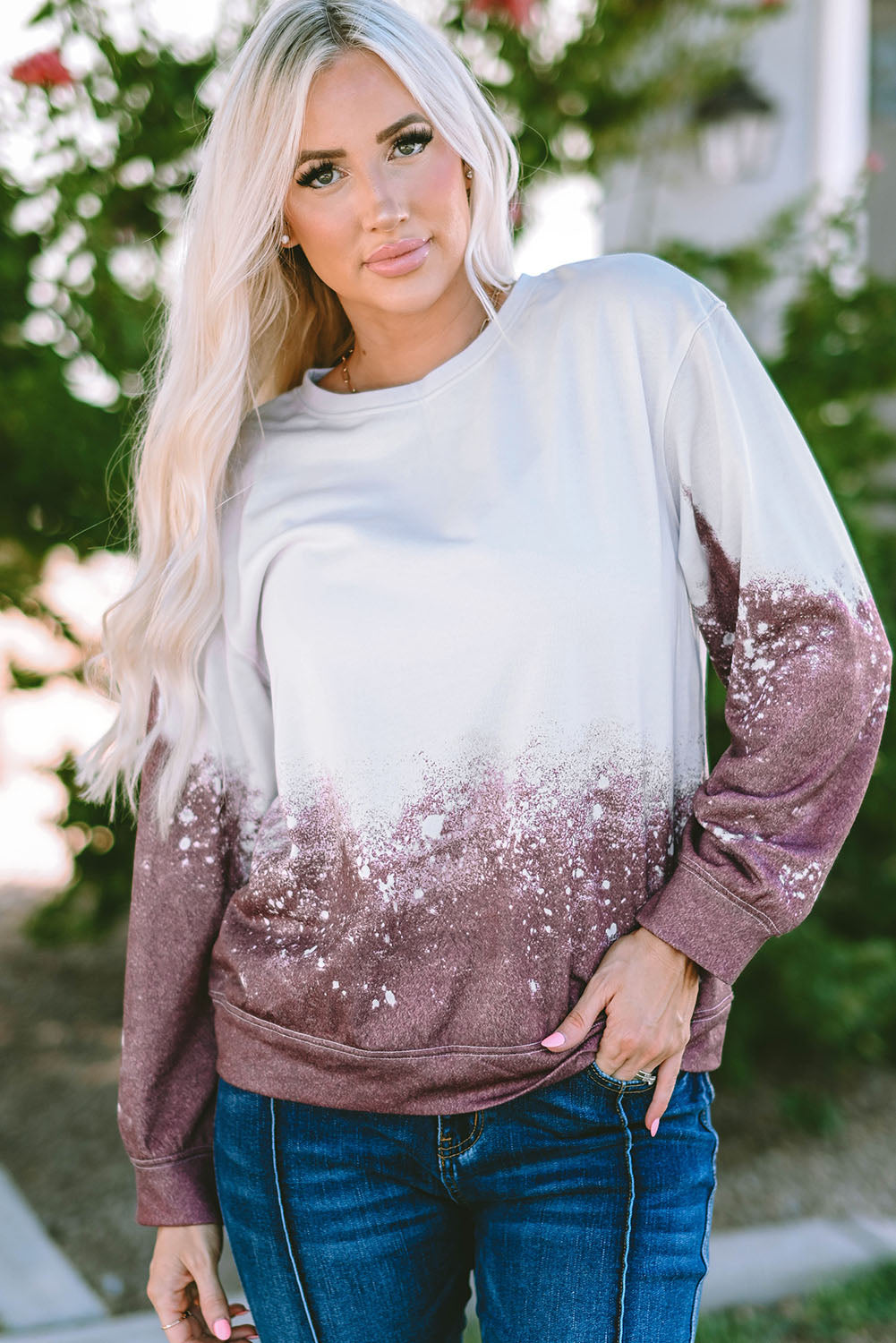 A person with long blonde hair is standing outdoors, facing away from the camera, wearing a Tie Dye Gradient Pullover Sweatshirt featuring a white and brown ombre splatter design.