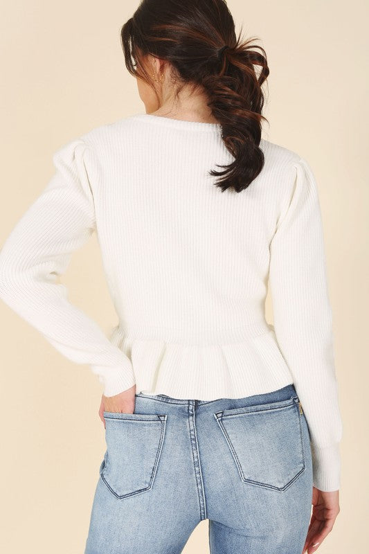 A woman stands elegantly in front of a white panel background, wearing the Peplum sweater top in red, featuring a round neck and puff sleeves, paired with a black skirt that has a side slit.