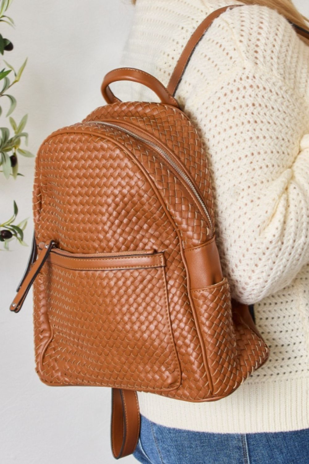 A person wearing a cream sweater and blue jeans carries the SHOMICO PU Leather Woven Backpack, showcasing exquisite craftsmanship with its woven design.