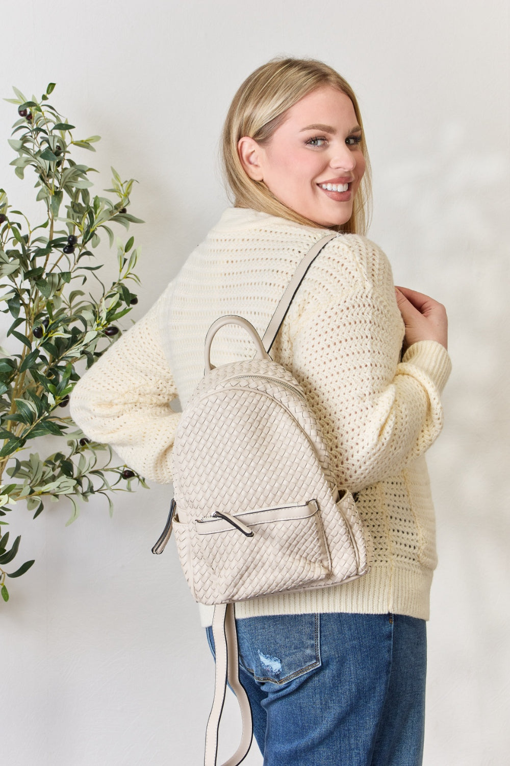 A person wearing a cream sweater and jeans is carrying the SHOMICO PU Leather Woven Backpack in brown.