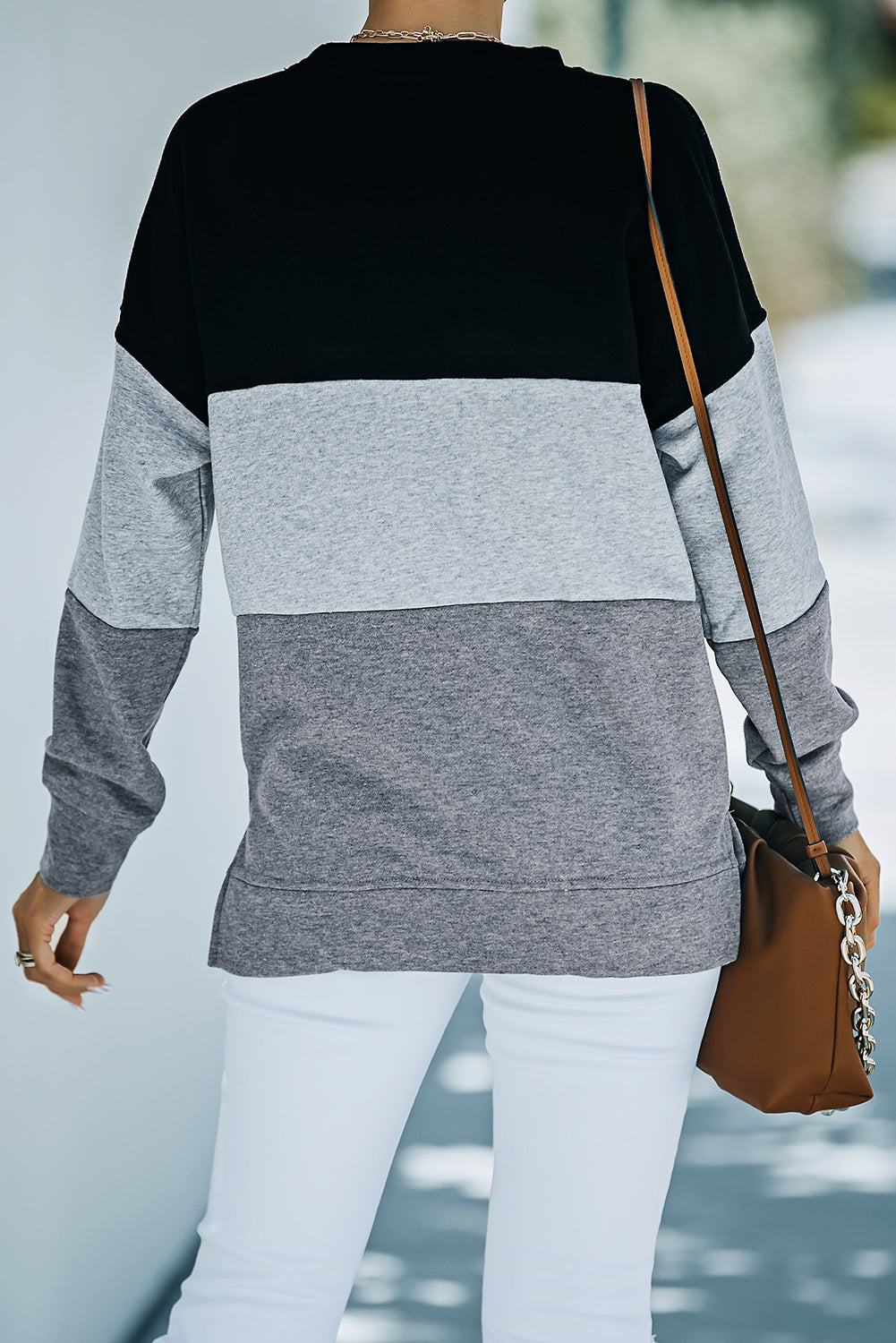 A person wearing a Colorblock Black Contrast Stitching Sweatshirt with Slits featuring black, gray, and light gray stripes, paired with white pants that resemble leggings and carrying a brown bag, shown from behind.