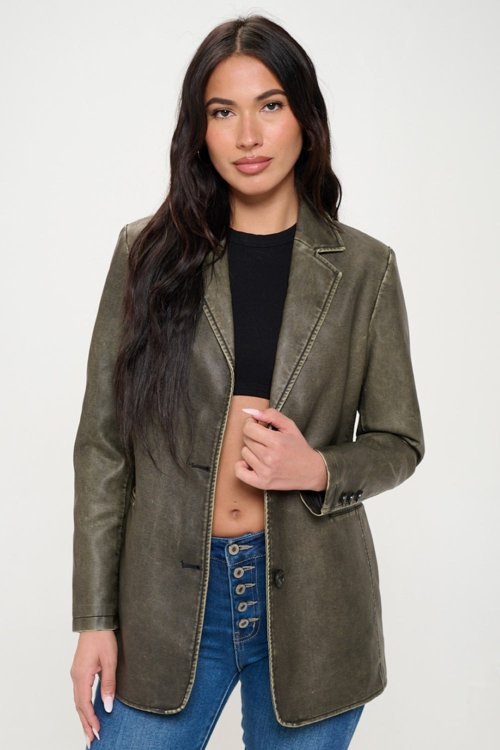 A person with long dark hair wears the Coalition LA Single-Breasted Vegan Leather Blazer in olive green over a black crop top and blue jeans against a neutral background, showcasing a stylish and ethical fashion choice.