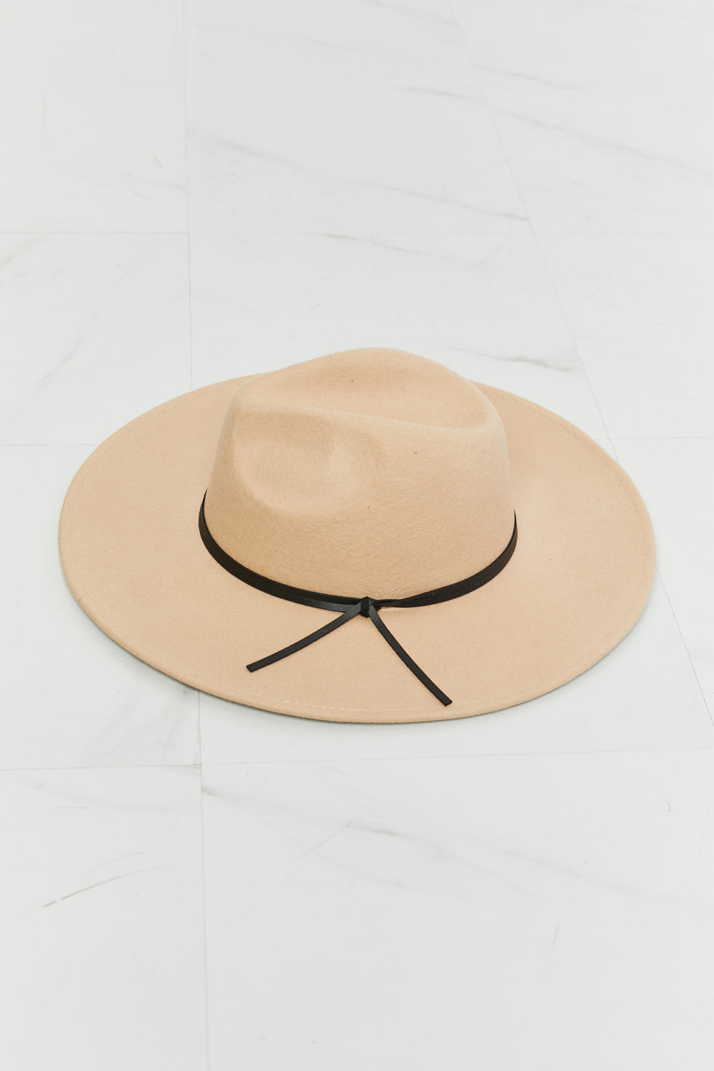 Wearing the Fame Make It Work Fedora Hat in light beige with faux leather detailing and a white tank top, a person smiles slightly while tilting their hat with one hand.