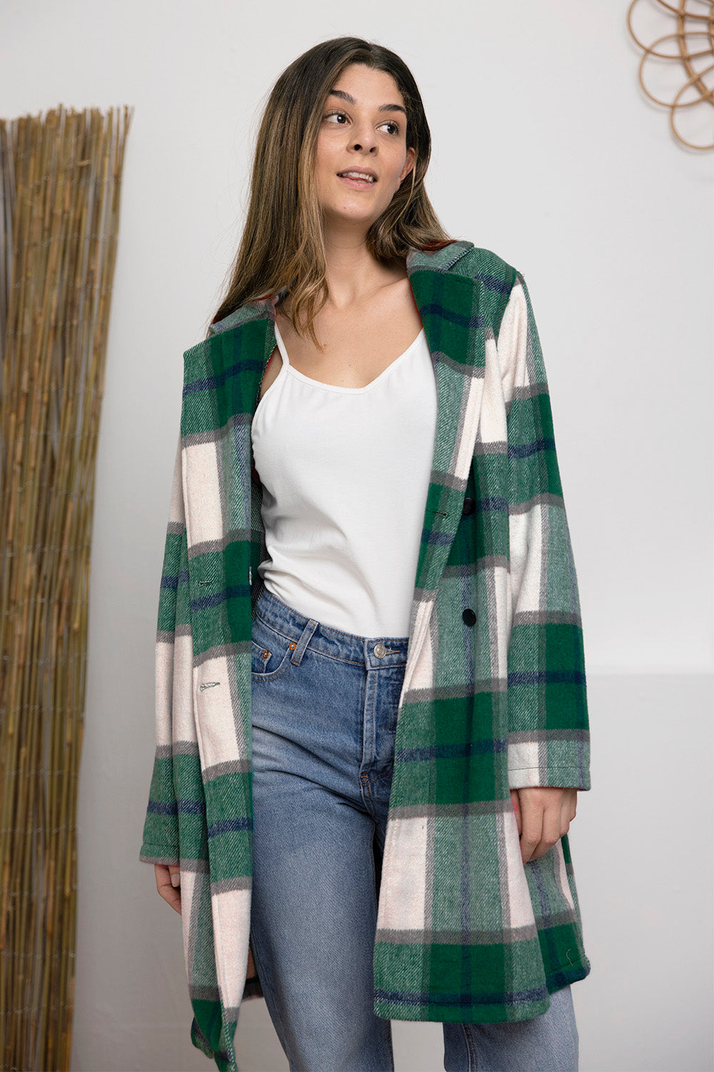 A woman stands on a sidewalk wearing the Double Take Full Size Plaid Button Up Lapel Collar Coat in pink and white over a white top and blue jeans, with her right hand lightly touching her hair. The polyester fabric of the coat makes it durable and perfect for an easy machine wash cold.