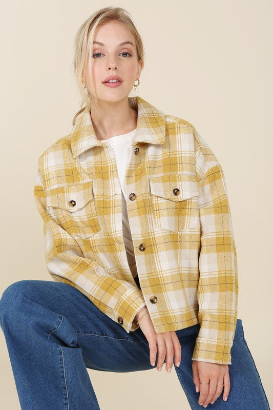 A person wearing a yellow plaid short shacket with pockets and blue jeans, highlighted by a crisp shirt collar, sits against a neutral backdrop.