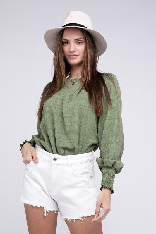 A woman wearing a Textured Shirred Yoke Top with bishop sleeves, complemented by a white hat and white shorts, stands against a plain background.