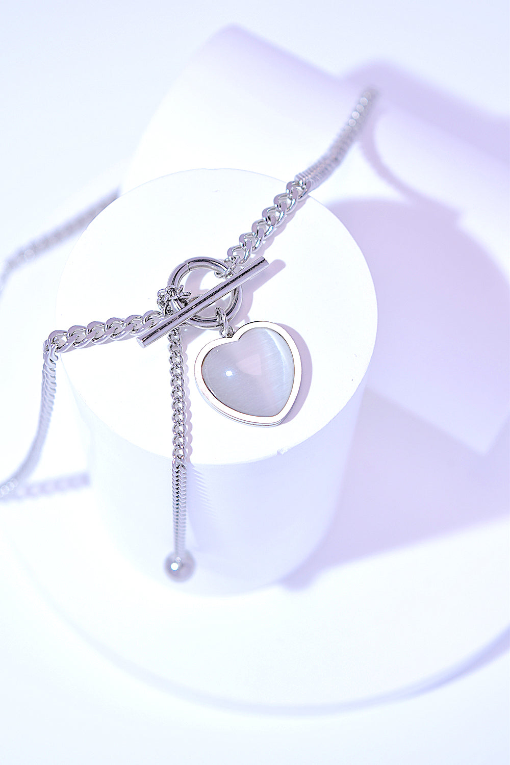 A Titanium Steel Heart Necklace with a heart-shaped pendant and a small key charm, featuring a delicate cat's eye stone, on a white background.