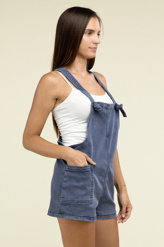 A person wearing the Washed Knot Strap Romper and a white tank top stands against a plain background.