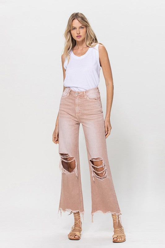 Person wearing 90's Vintage Crop Flare Jeans in rose pink with high waist, distressed details, rips on the knees, and frayed hems, paired with beige strappy sandals.