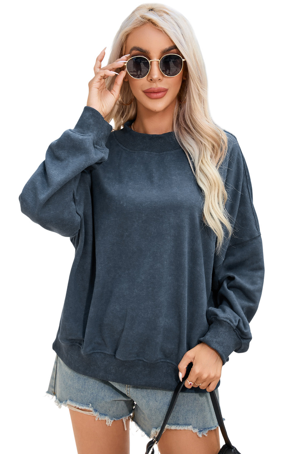 A person with long blonde hair is wearing a sky blue drop shoulder crew neck pullover sweatshirt and light denim shorts, standing outdoors with their back to the camera.