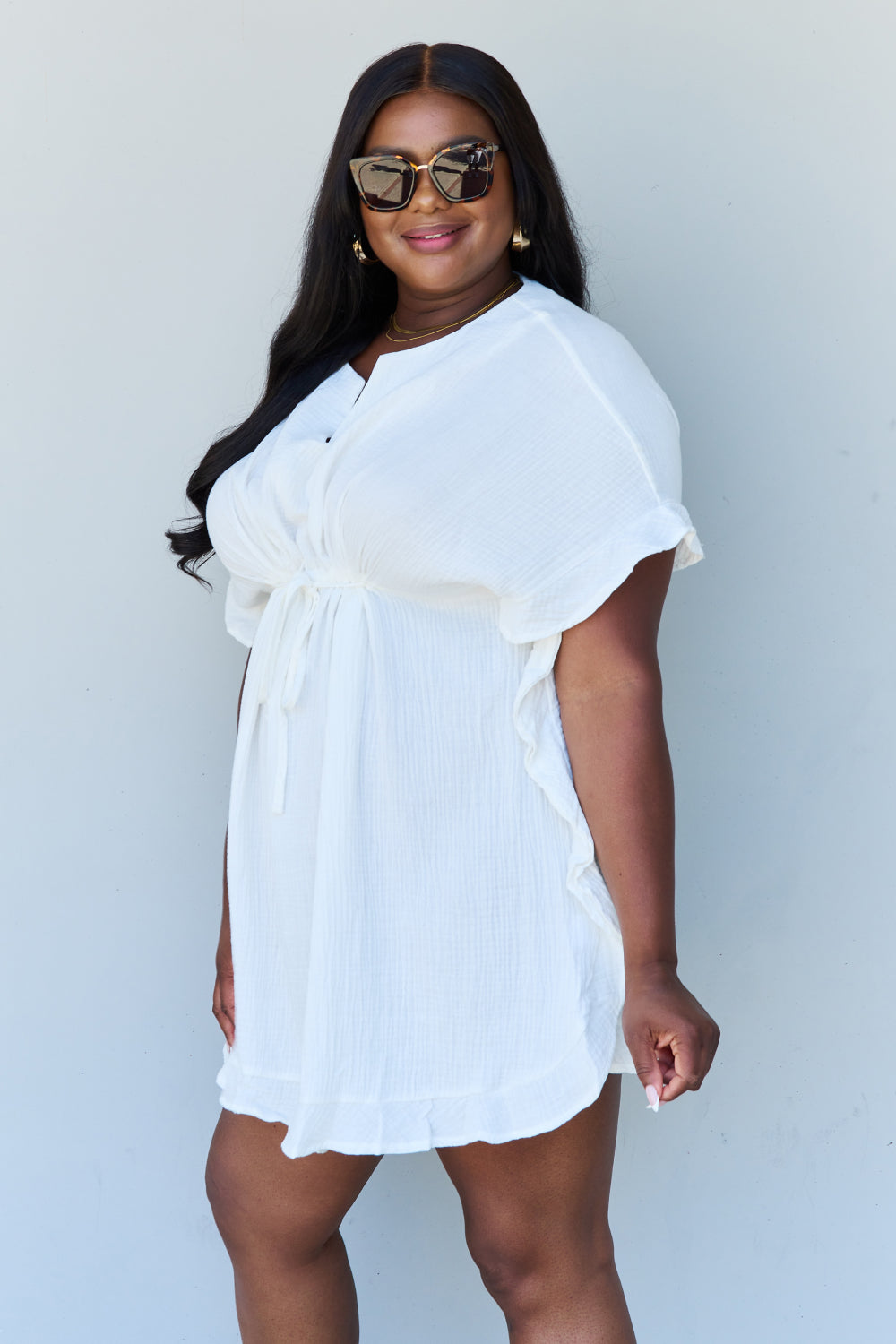 A person with long dark hair smiles while posing in the Ninexis Out Of Time Full Size Ruffle Hem Dress with Drawstring Waistband in White against a plain background.