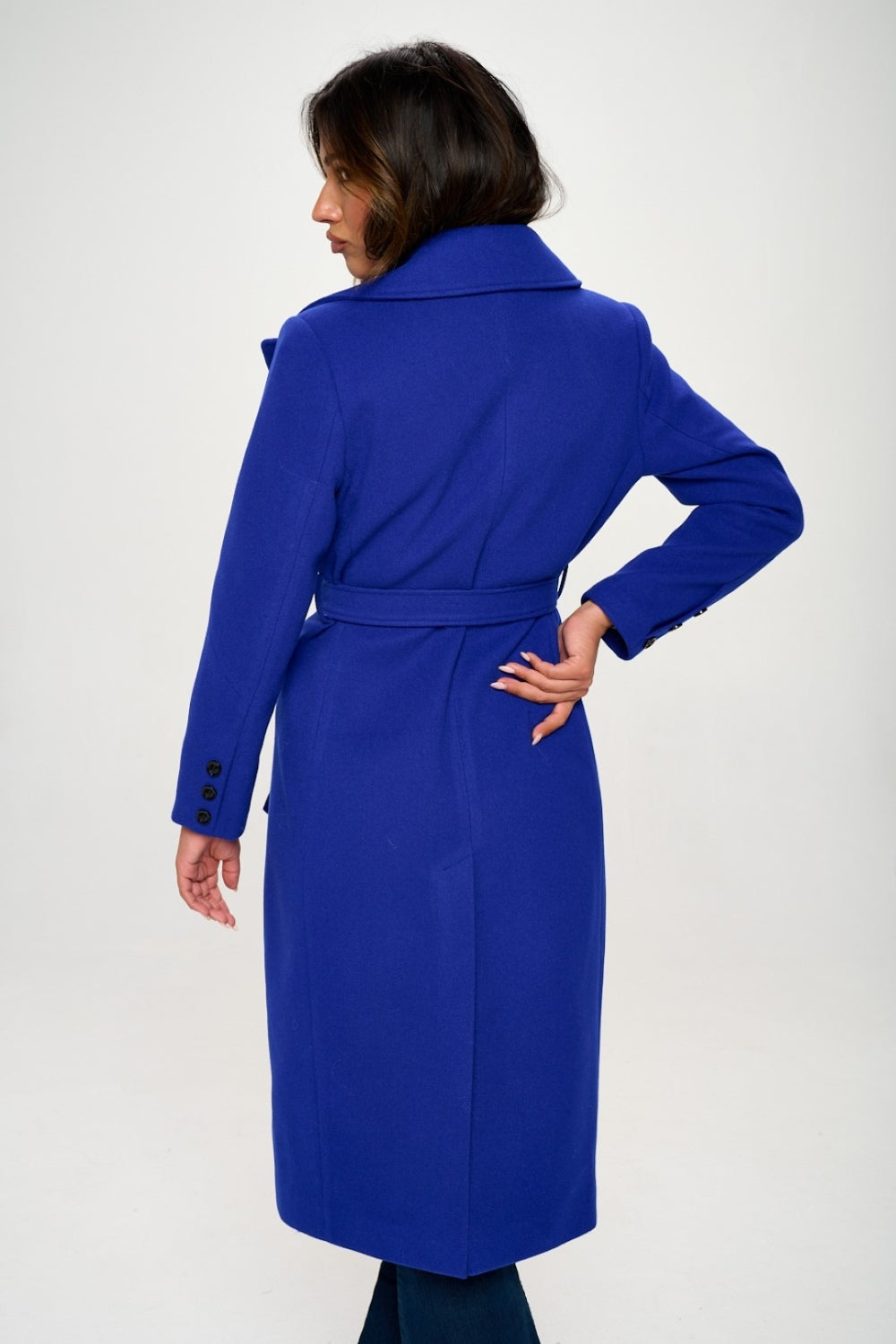 Person wearing the Coalition LA Double-Breasted Longline Coat with Belt, made from vegan wool in blue, over a grey turtleneck, posing against a plain background.