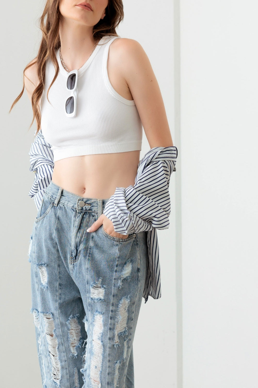 A person wearing Litz La Washed Barrel Leg High Waist Distressed Jeans and white sandals stands on a gray floor against a white wall.