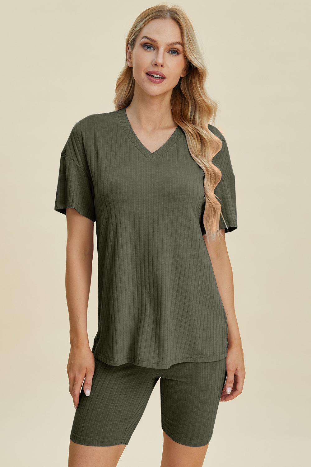 A woman with long blonde hair wearing the Basic Bae Full Size Ribbed V-Neck Short Sleeve Top and Shorts Set in rust stands against a plain background. This stylish two-piece set is made from a comfortable, stretchy fabric that is also machine washable.