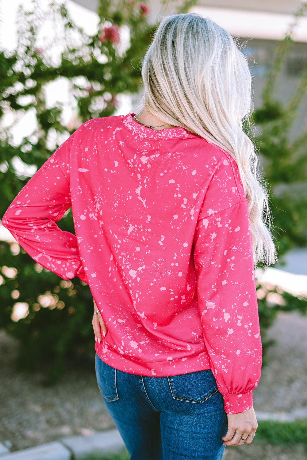 Person with long blonde hair wearing a Rose Tie Dye Long Sleeve Pullover Sweatshirt and blue jeans, standing outdoors with back to the camera.