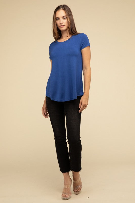 A person with long hair is wearing a blue Flowy Round Hem Rayon Short Sleeve Top and black pants, standing against a plain beige background.