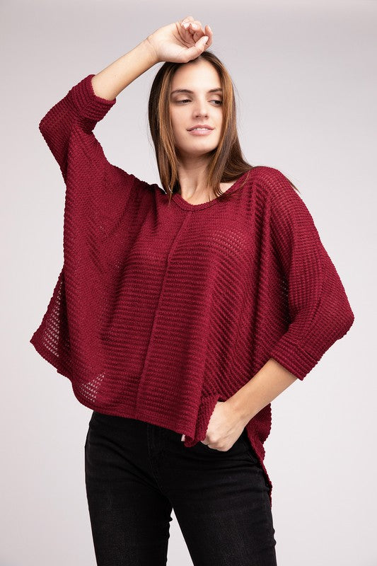 A woman in a 3/4 Sleeve V-Neck Hi-Low Hem Jacquard Sweater and black jeans, posing with one arm raised, eyes closed, against a light gray background.