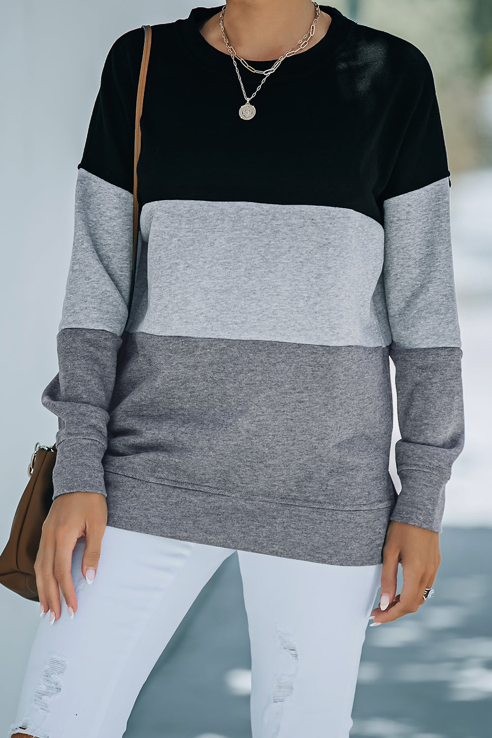 A person wearing a Colorblock Black Contrast Stitching Sweatshirt with Slits featuring black, gray, and light gray stripes, paired with white pants that resemble leggings and carrying a brown bag, shown from behind.