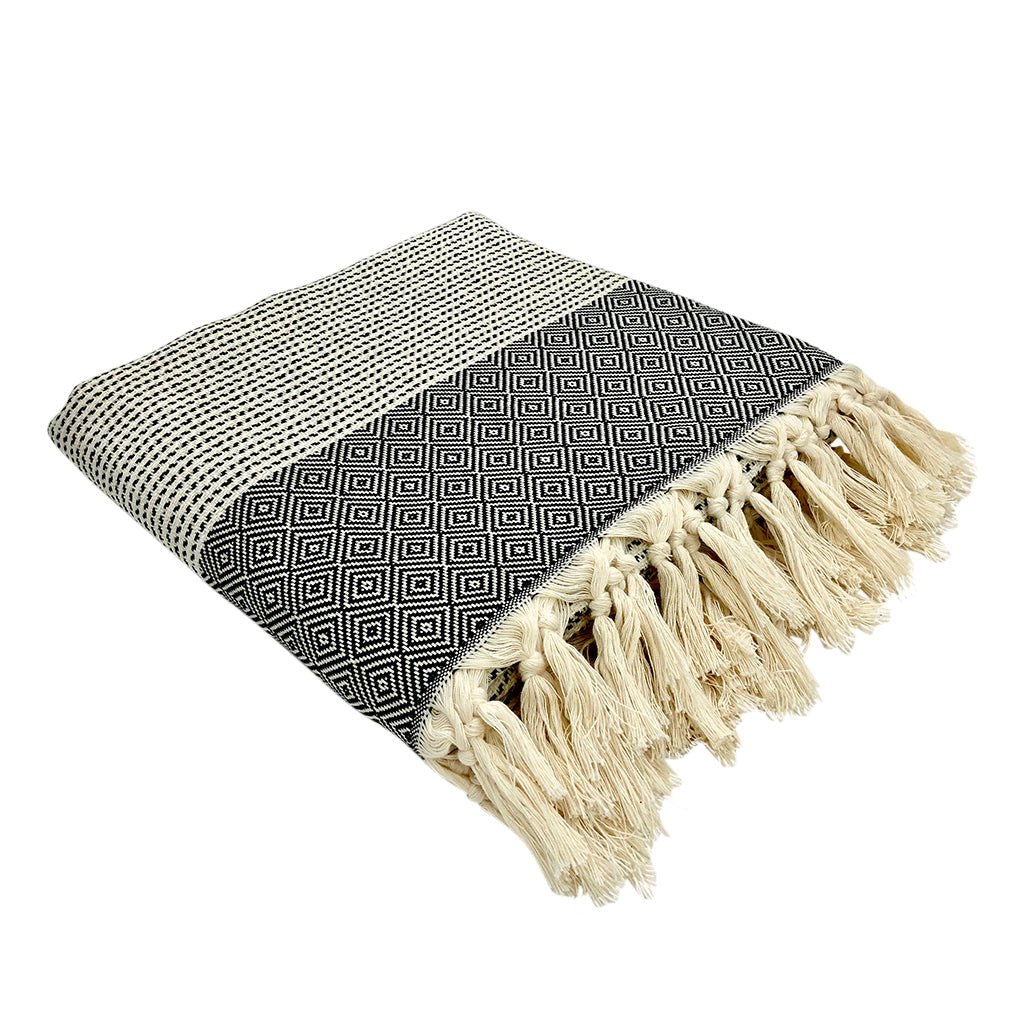 The Diamond Stripe Turkish Throw, in black and white, showcases a geometric diamond pattern and is accented with hand-knotted fringe at the edge, providing both style and comfort.