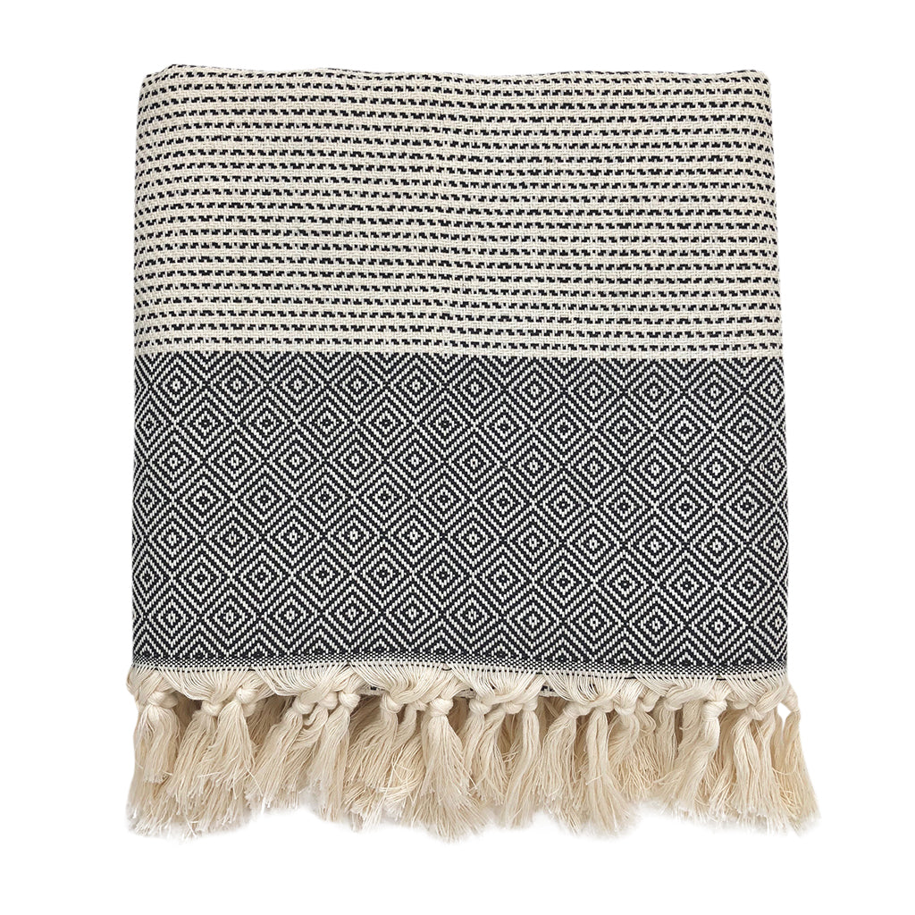 The Diamond Stripe Turkish Throw, in black and white, showcases a geometric diamond pattern and is accented with hand-knotted fringe at the edge, providing both style and comfort.