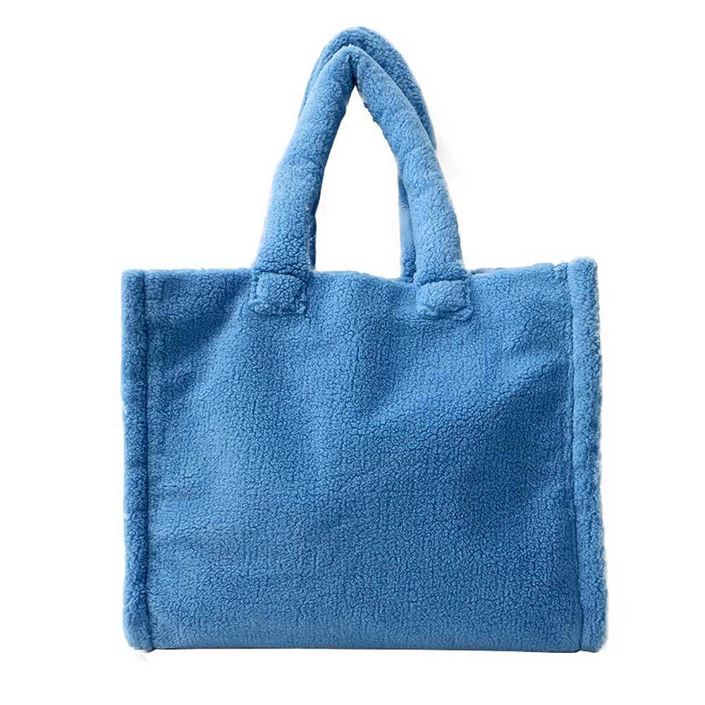 The Astrid Shopper Tote is a tote bag made from cozy blue teddy fleece. It showcases a straightforward rectangular shape with two sturdy handles and comes equipped with a zippered interior pocket for extra functionality.