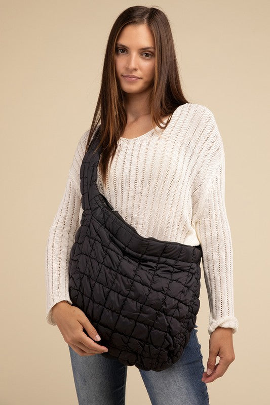 Woman in a white sweater and jeans holding a large black Puff Quilted Crossbody Shoulder Bag.