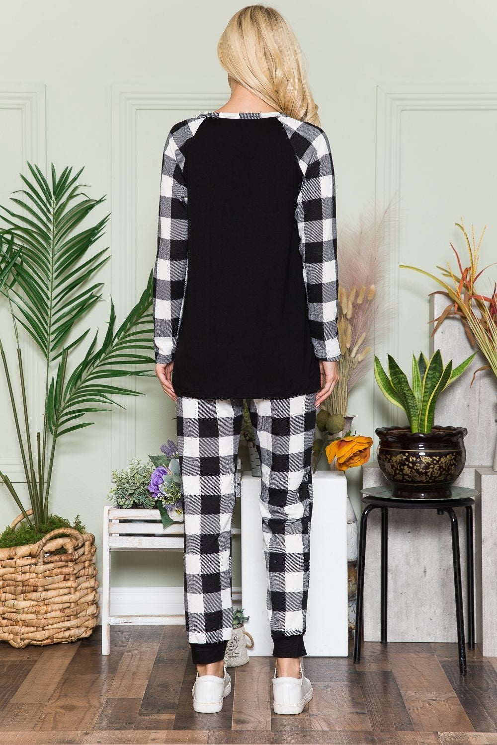 A person wearing the Celeste Plaid Long Sleeve T-Shirt with Pockets stands in a room filled with plants and wooden flooring, presenting a laid-back style.