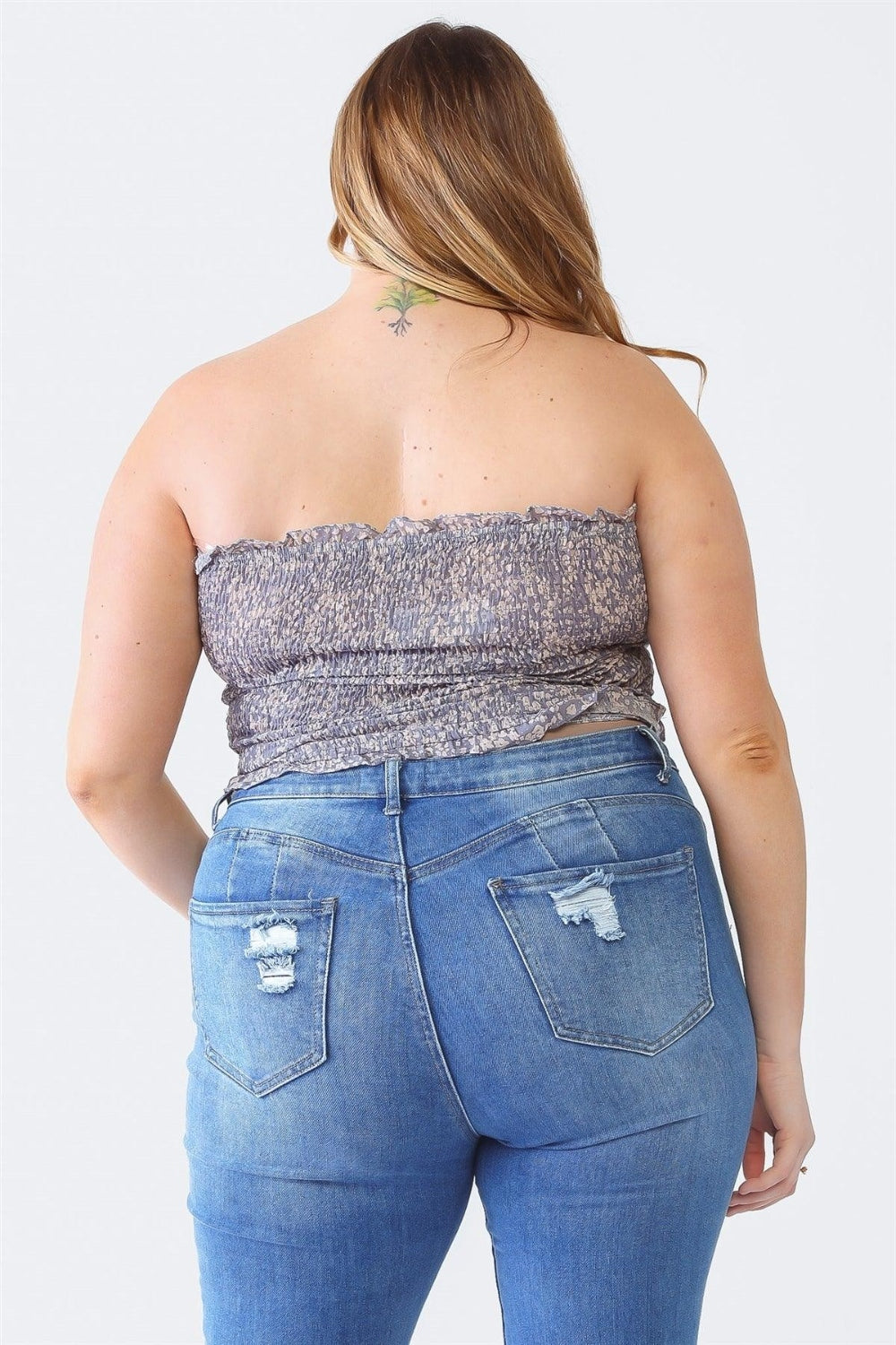 A person with long hair is wearing the Zenobia Plus Size Drawstring Smocked Floral Tube Top paired with ripped jeans, standing against a plain background—a perfect addition to any summer wardrobe.