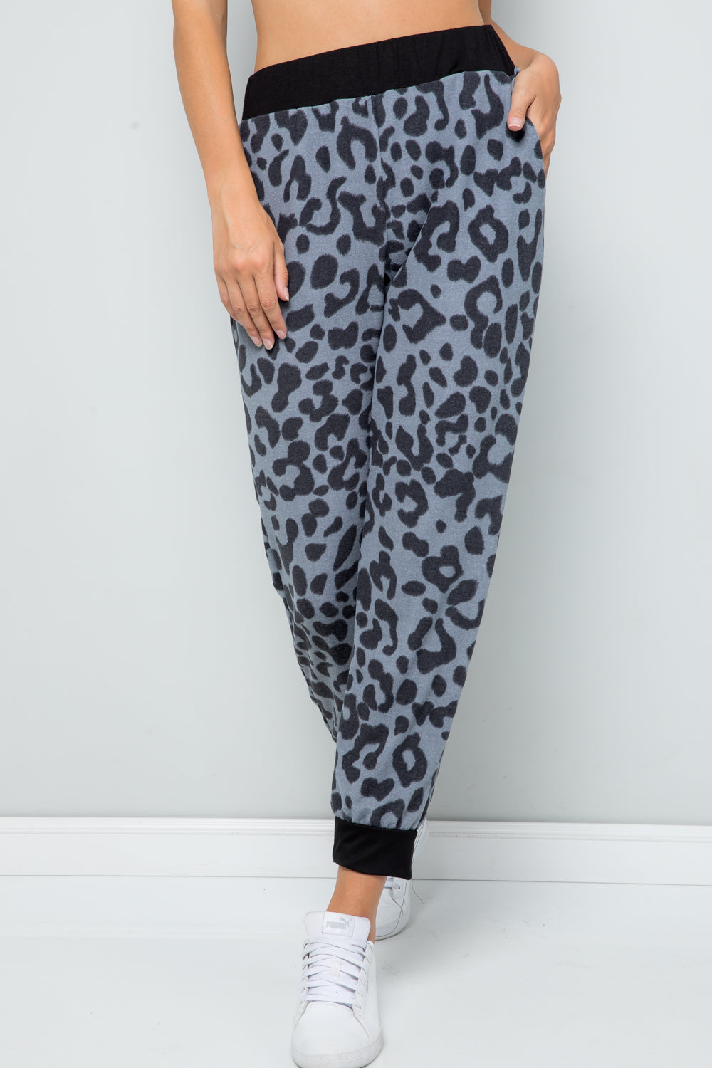 Person wearing Celeste Full Size Leopard Contrast Sweatpants with a black waistband and cuffs, paired with white sneakers, against a plain light gray background.