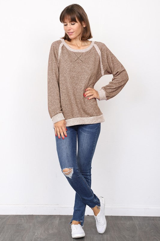 A woman with brown hair stands against a white background, looking sideways while wearing the Shimmer French Terry Top in gray paired with blue jeans.