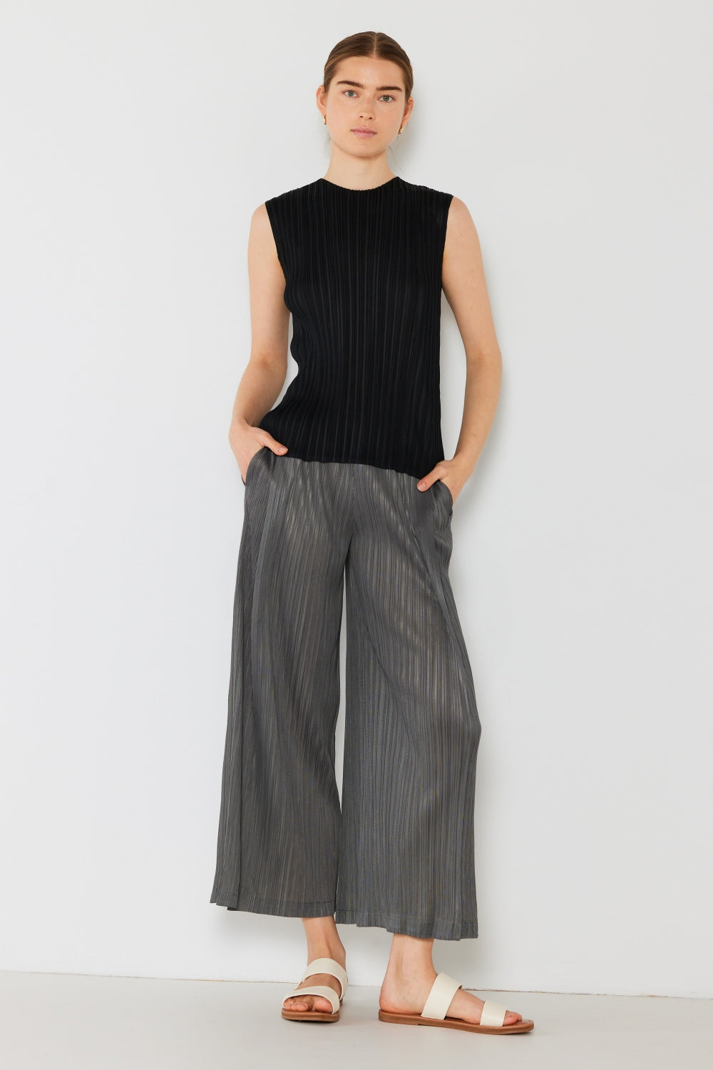 A person wearing the Marina West Swim Pleated Wide-Leg Pants with side pleat detail in red, standing against a white background with hands in pockets and wearing white sandals.