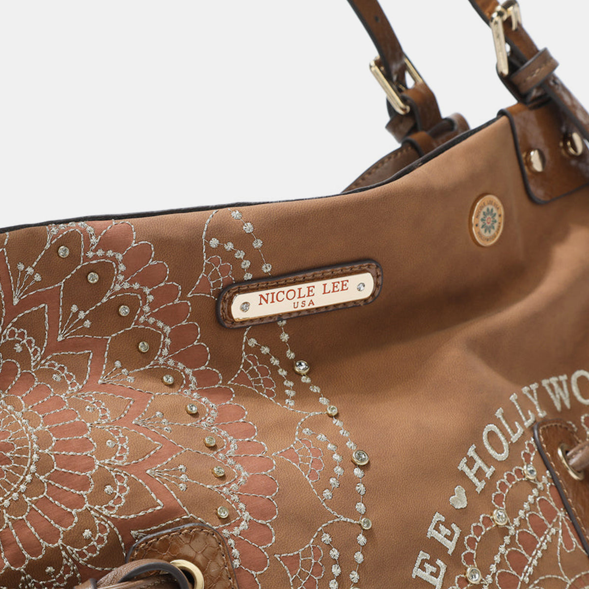 The Nicole Lee USA Side Braided Tassel Inlaid Rhinestone Embroidery Hobo Bag features intricately designed white mandala patterns on brown vegan leather, along with "Nicole Lee Hollywood USA" text. It includes top handles and decorative braided accents, as well as adjustable dual shoulder straps for added versatility.