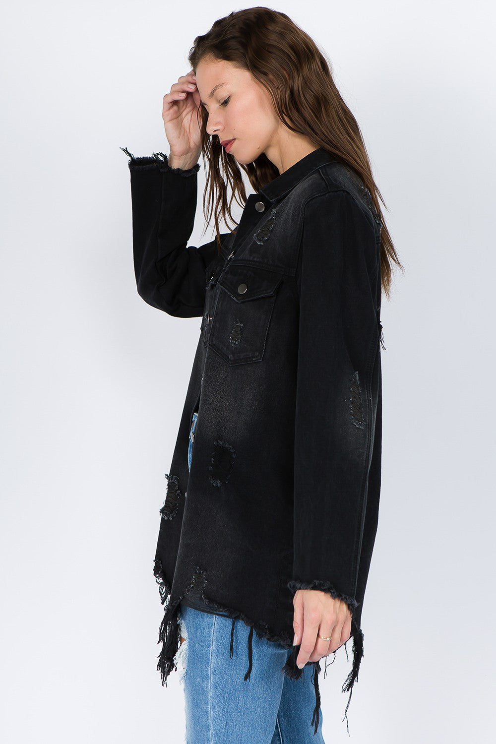 A woman wearing the American Bazi Distressed Frayed Hem Denim Jacket over a white top and ripped blue jeans stands against a plain background, giving her outfit a vintage feel.