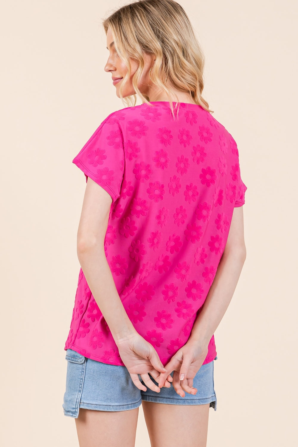 A woman poses against a neutral background, effortlessly styled in the BOMBOM Textured Floral Pattern Short Sleeve T-Shirt, a bright pink top that complements her denim shorts perfectly.