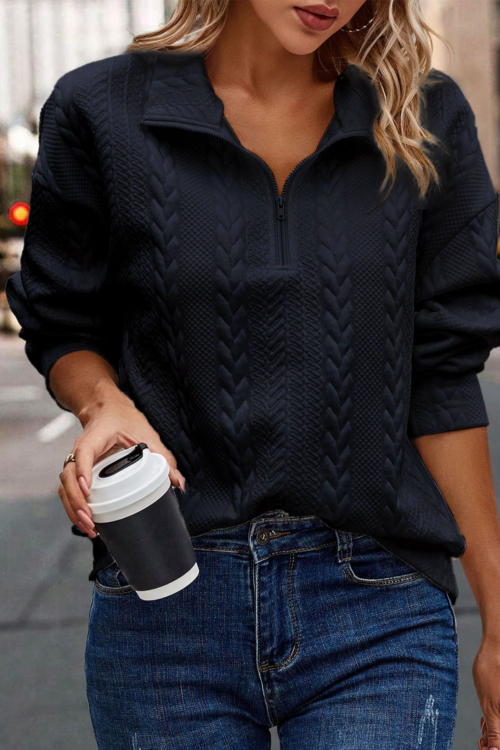 A person wearing a Navy Blue Zip Up Cable Textured Sweatshirt and blue jeans, seen from the back, standing on an urban street.