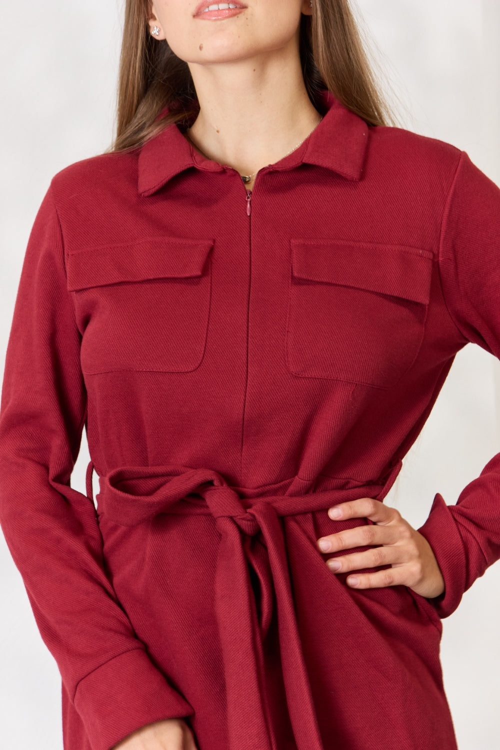 A woman wearing the Culture Code Full Size Tie Front Half Zip Long Sleeve Shirt Dress stands in front of a plain background next to a potted plant.