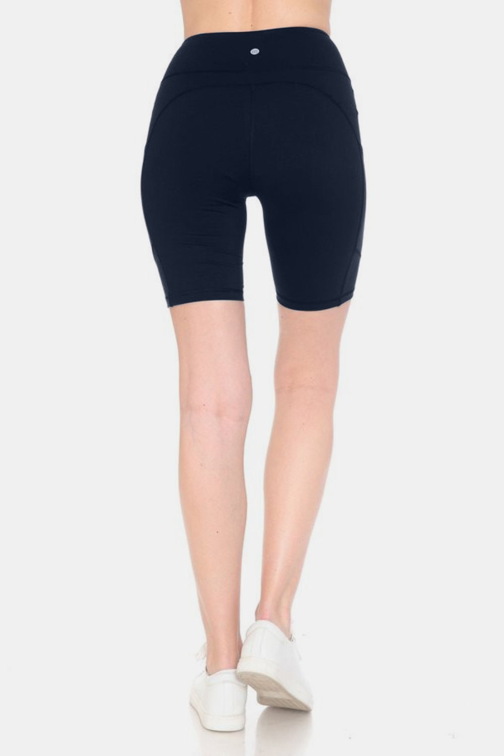 Person wearing Leggings Depot Full Size High Waist Active Shorts in black, made from moisture-wicking fabric, paired with white sneakers, standing upright against a neutral background.