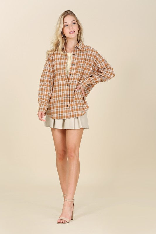 Wearing an Autumn beige plaid shirt, a person with long hair complements their look with hoop earrings, showcasing the season's warm hues. This long-sleeved shirt rests gracefully against a beige backdrop and is ideal for machine wash cold care.