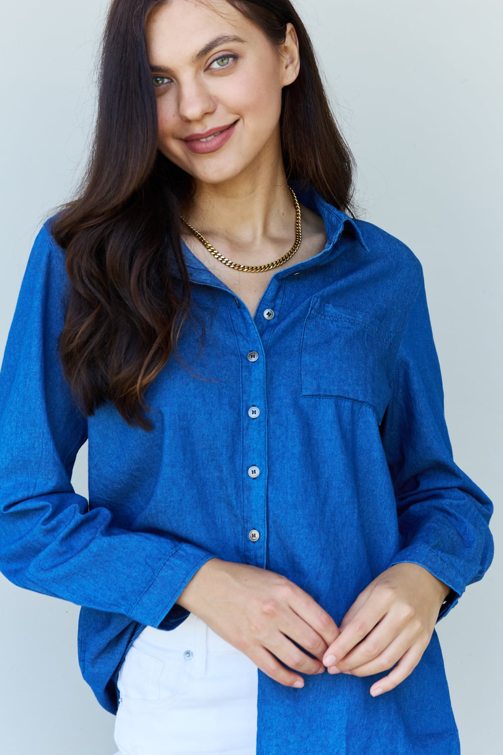 A person standing against a plain background, wearing the Doublju Blue Jean Baby Denim Button Down Shirt Top in Dark Blue and white shorts, smiling and holding a hand to their hair.