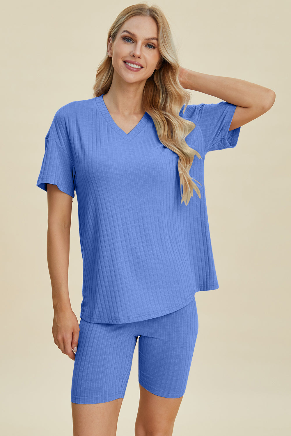 A woman with long blonde hair wearing the Basic Bae Full Size Ribbed V-Neck Short Sleeve Top and Shorts Set in rust stands against a plain background. This stylish two-piece set is made from a comfortable, stretchy fabric that is also machine washable.