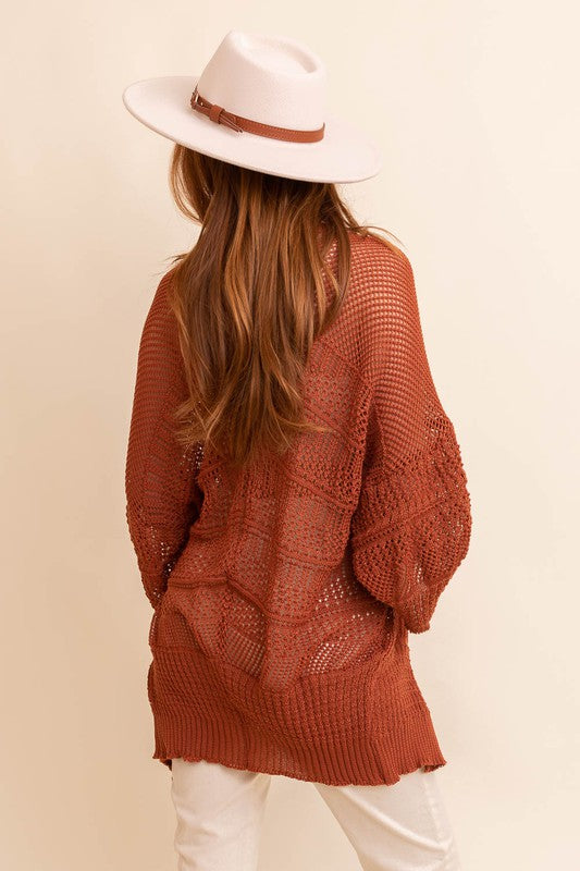 A person with long hair, wearing an oversized Knit Netted Cardigan, a crop top, and denim shorts, stands in a light-colored room.