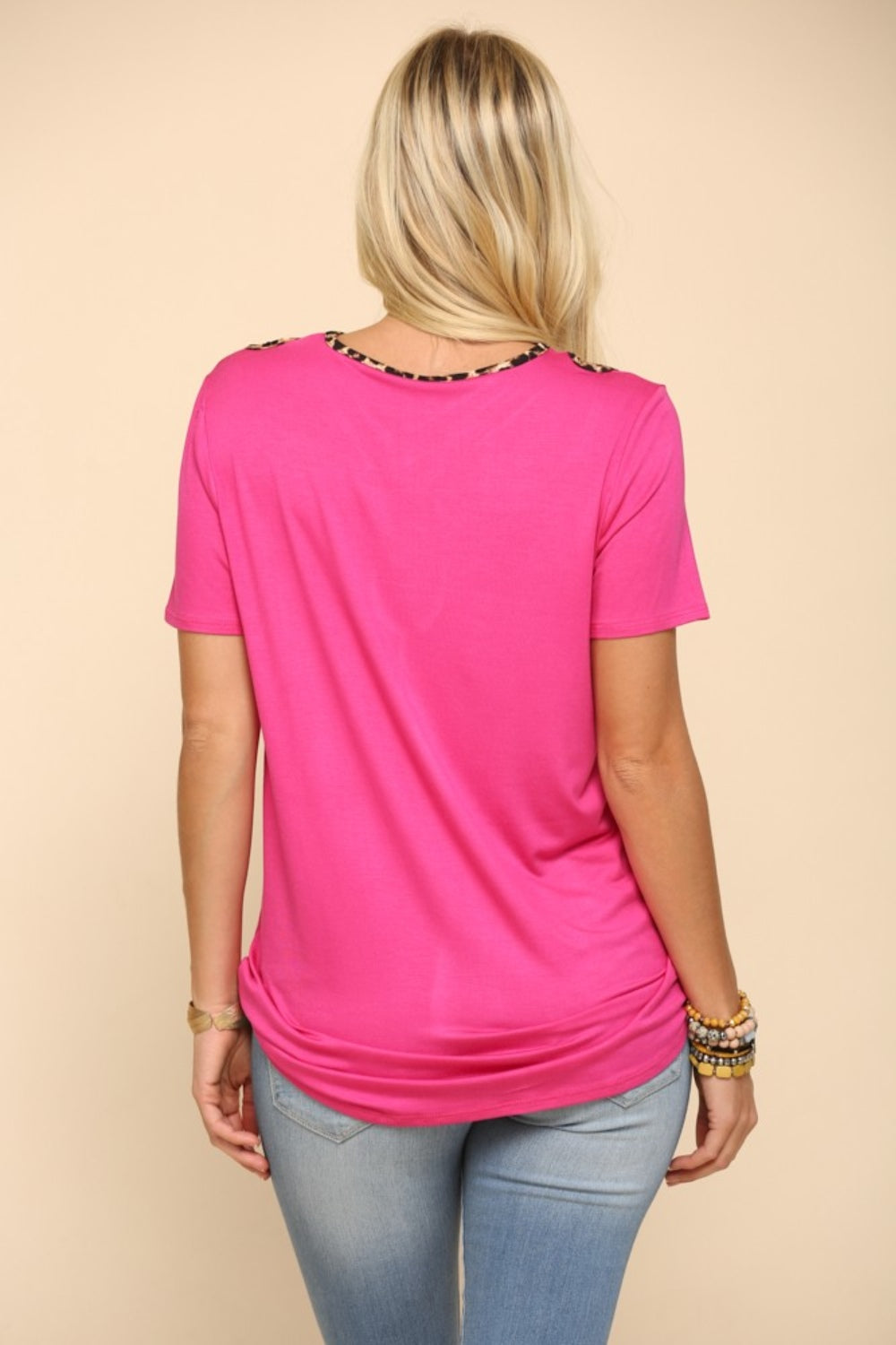 A person showcases the Celeste Full Size Crisscross Cutout Leopard Contrast Trim T-Shirt in bright pink, paired with light blue jeans, posing confidently against a beige background.