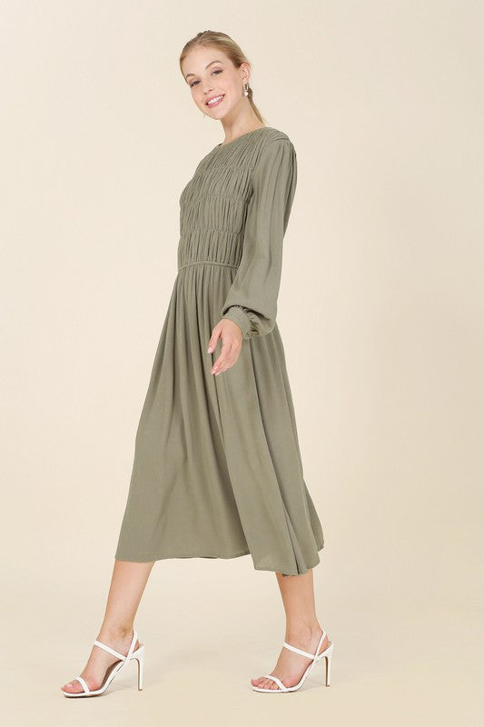 A woman in the green "Dressed Up Ruched Midi Dress," featuring a boat neck design and crafted from crinkle fabric.