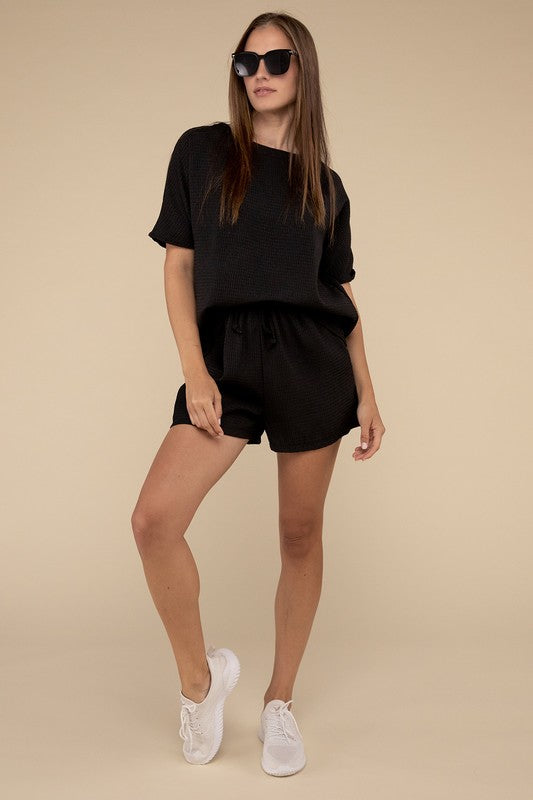 Clad in the Waffle Round Neck Top and Short Set paired with black sunglasses, a person stands against a plain beige background, highlighting the non-stretch polyester fabric.