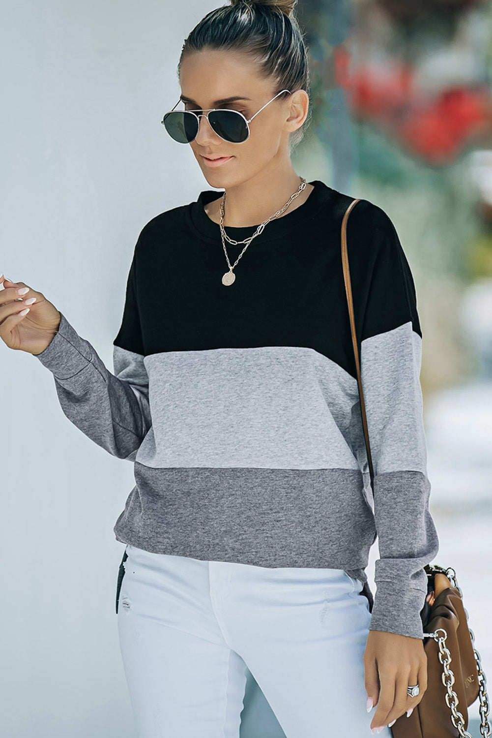 A person wearing a Colorblock Black Contrast Stitching Sweatshirt with Slits featuring black, gray, and light gray stripes, paired with white pants that resemble leggings and carrying a brown bag, shown from behind.