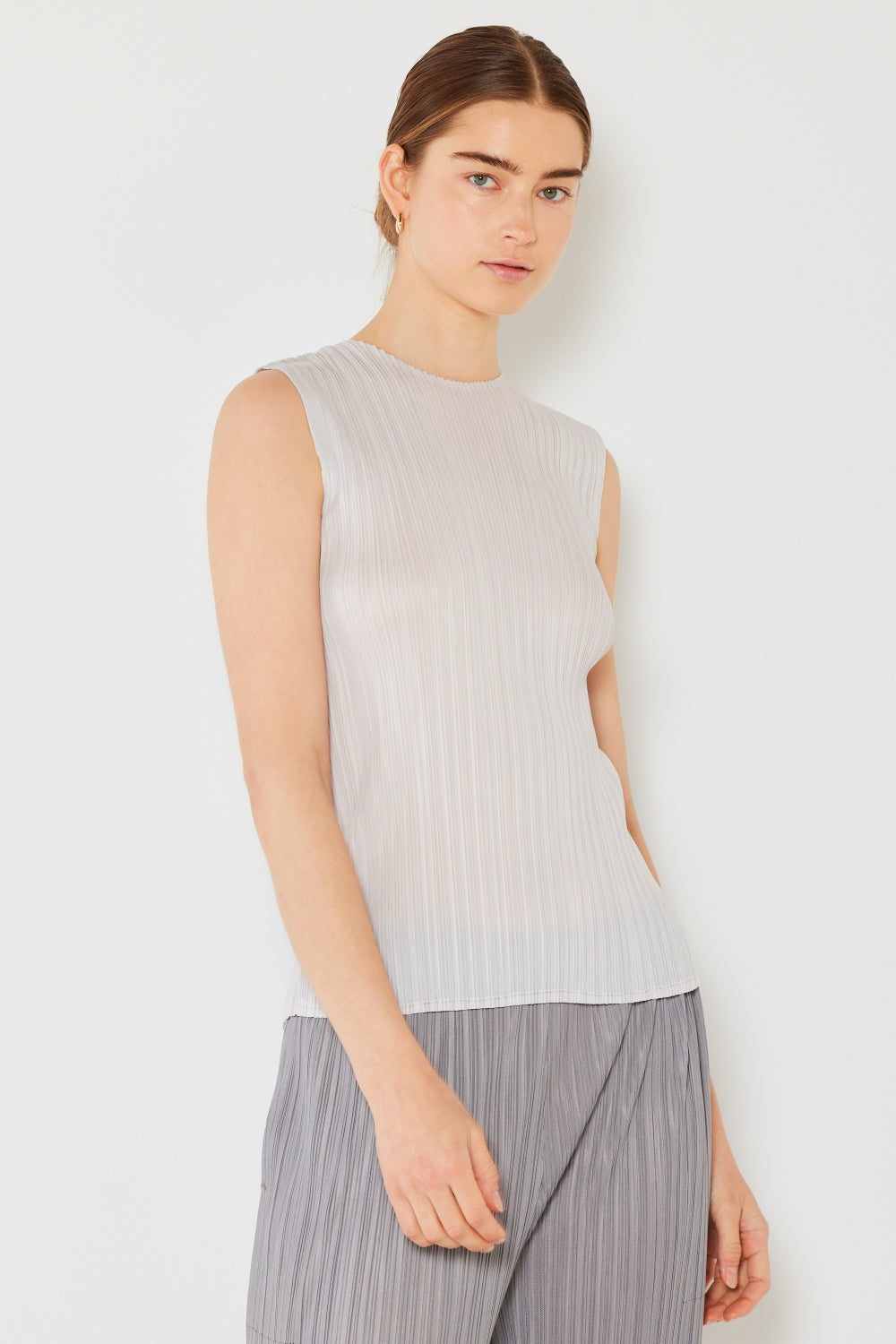 Person wearing a Marina West Swim Pleated Sleeveless Crewneck Tank and a gray pleated skirt, standing against a white background.