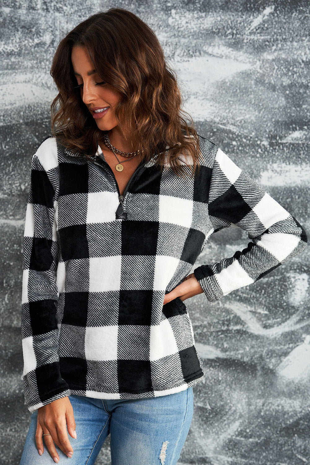 A woman with wavy hair is wearing a cozy Black Plaid Print 1/4 Zip Turn-down Collar Sweatshirt and blue jeans, standing with her back to the camera against a textured gray background.