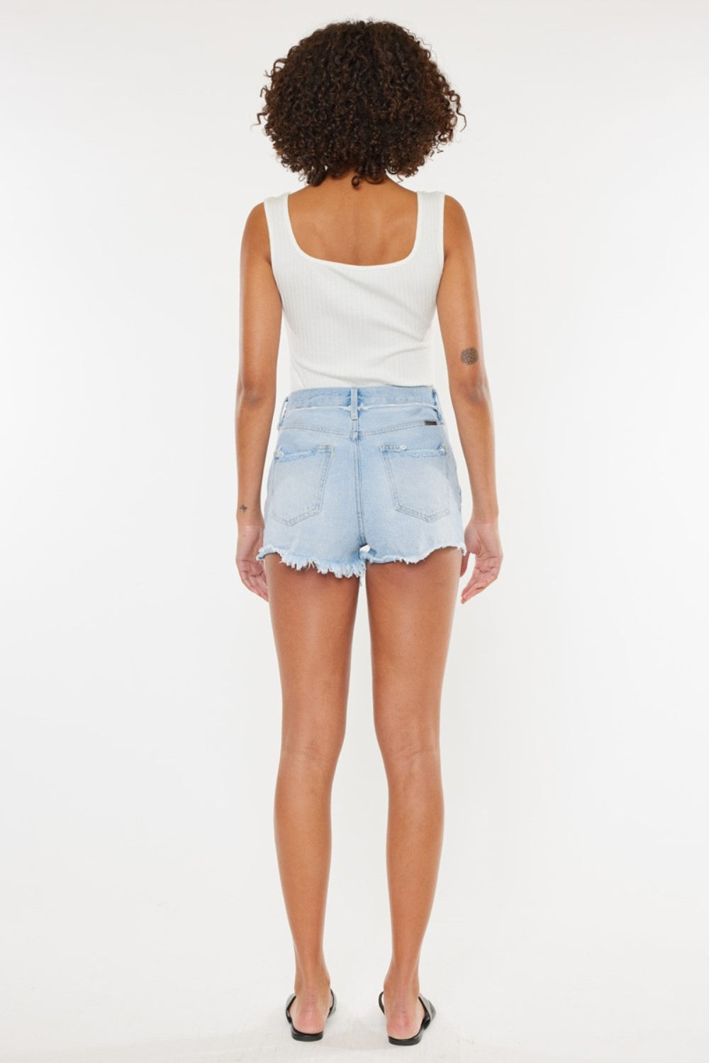 A person wearing a white tank top and Kancan Distressed Button Fly Denim Shorts poses against a plain background, showcasing a quintessential summer wardrobe staple.